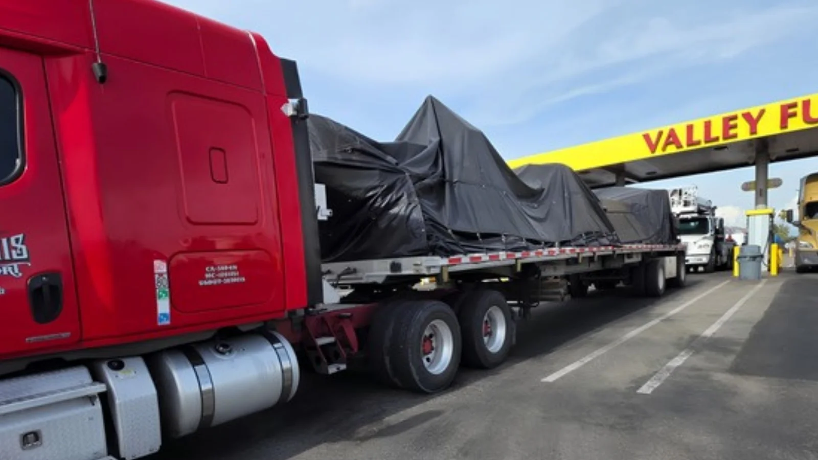 Red semi truck hauling tarped machinery on a flatbed