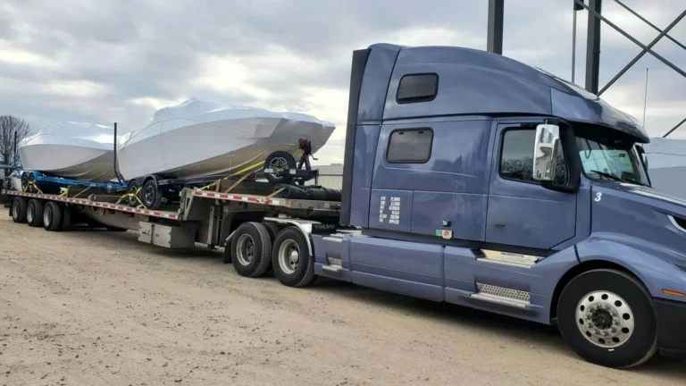 Semi truck hauling shrink-wrapped boats on a step deck trailer