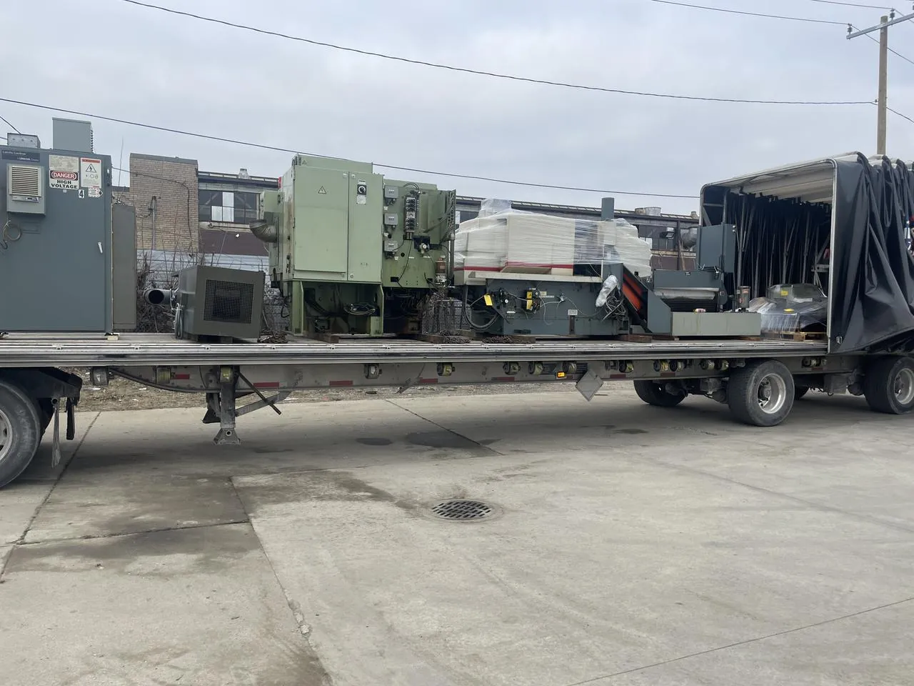Several industrial machines on a Conestoga flatbed deck with the tarp kit rolled to the rear