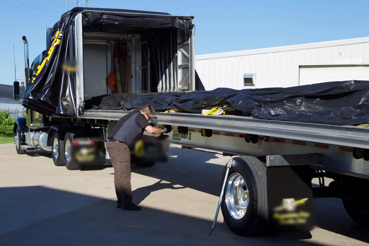 Driver securing freight on a Conestoga flatbed with the rolling tarp kit pulled to the front