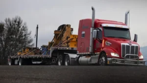 Red semi-truck hauling heavy yellow industrial equipment on a step deck trailer