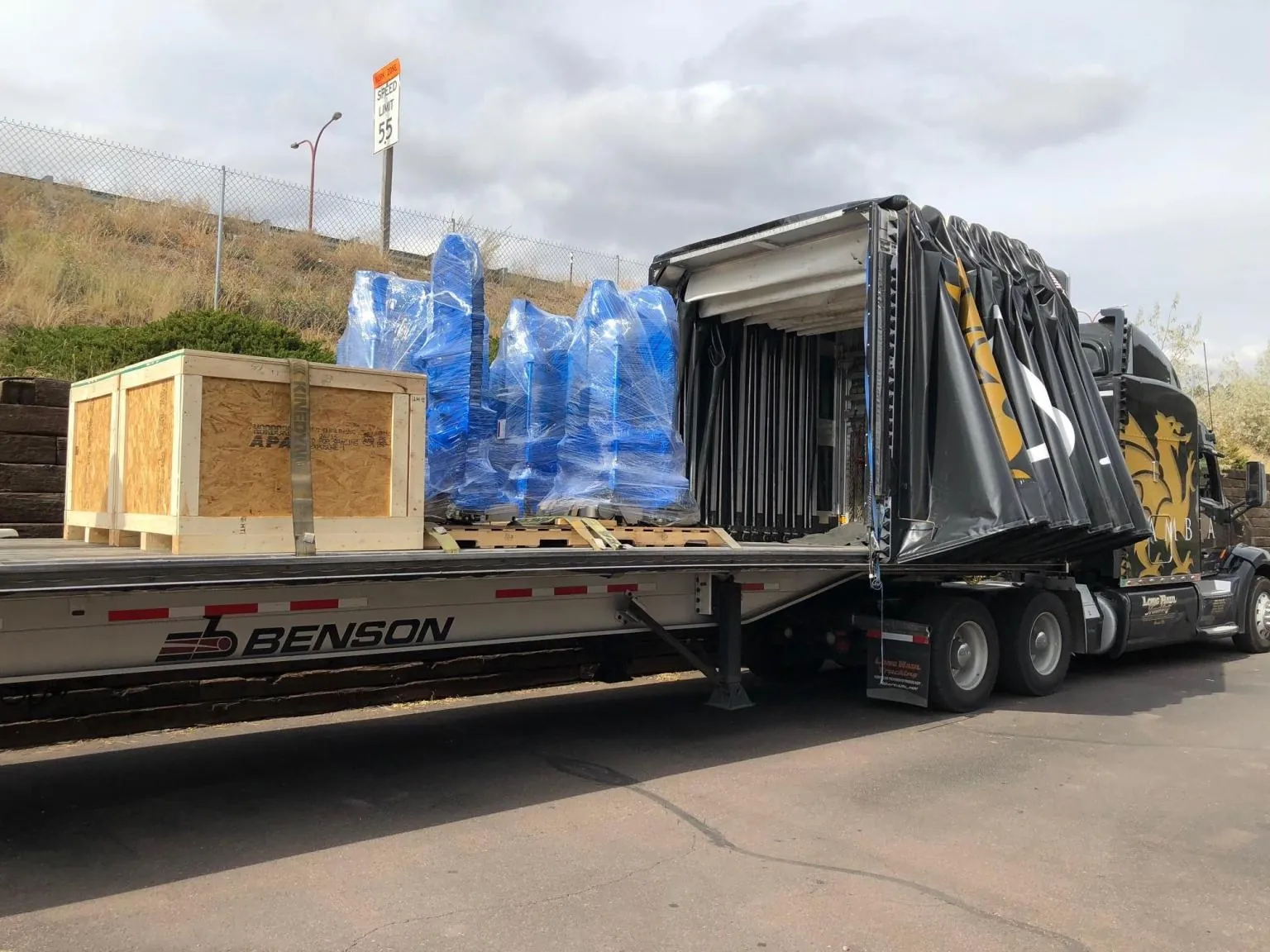 Wood machine crate and blue shrink wrapped equipment from different shippers sharing a Conestoga trailer
