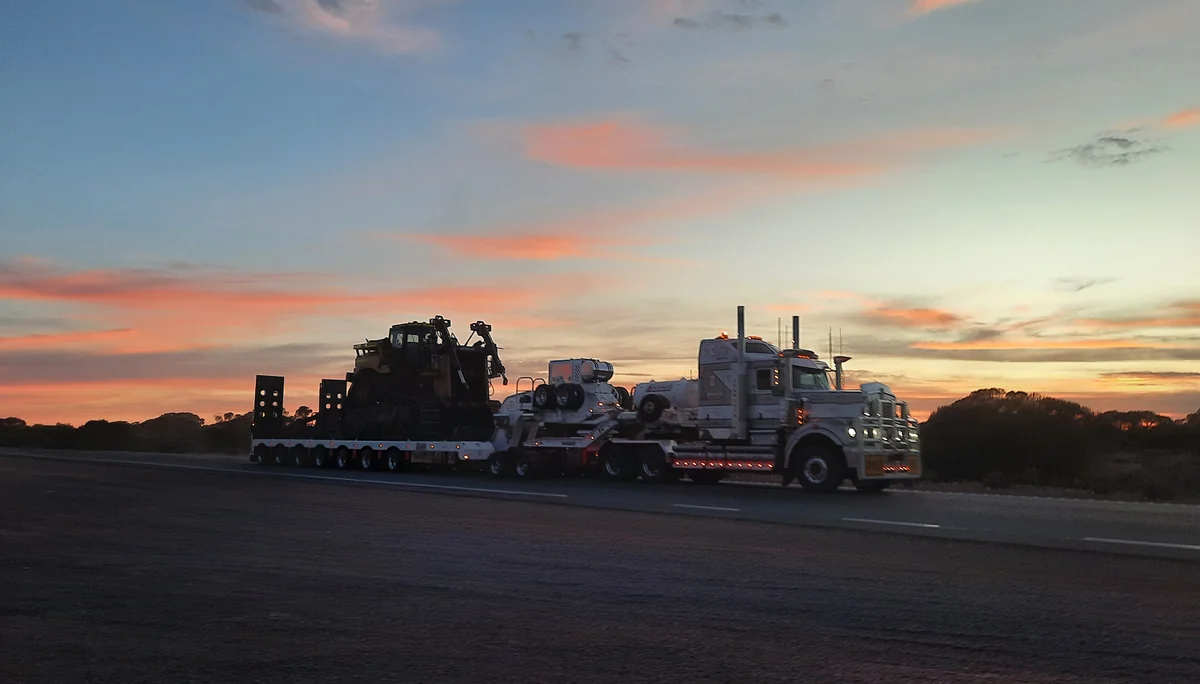 Crawler dozer loaded on a multi axle lowboy trailer behind a heavy haul truck at sunset