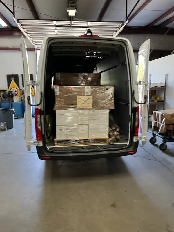 Expedited roofing materials delivery: sprinter van with rear doors open and a shrink wrapped pallet of cartons and tubes