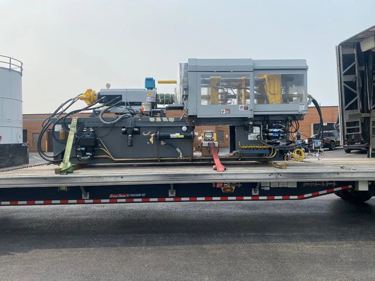 Injection molding machine chained on a flatbed trailer deck with dunnage underneath