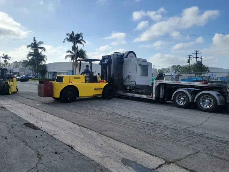 Forklift loading a CNC machine onto a double drop trailer in Los Angeles