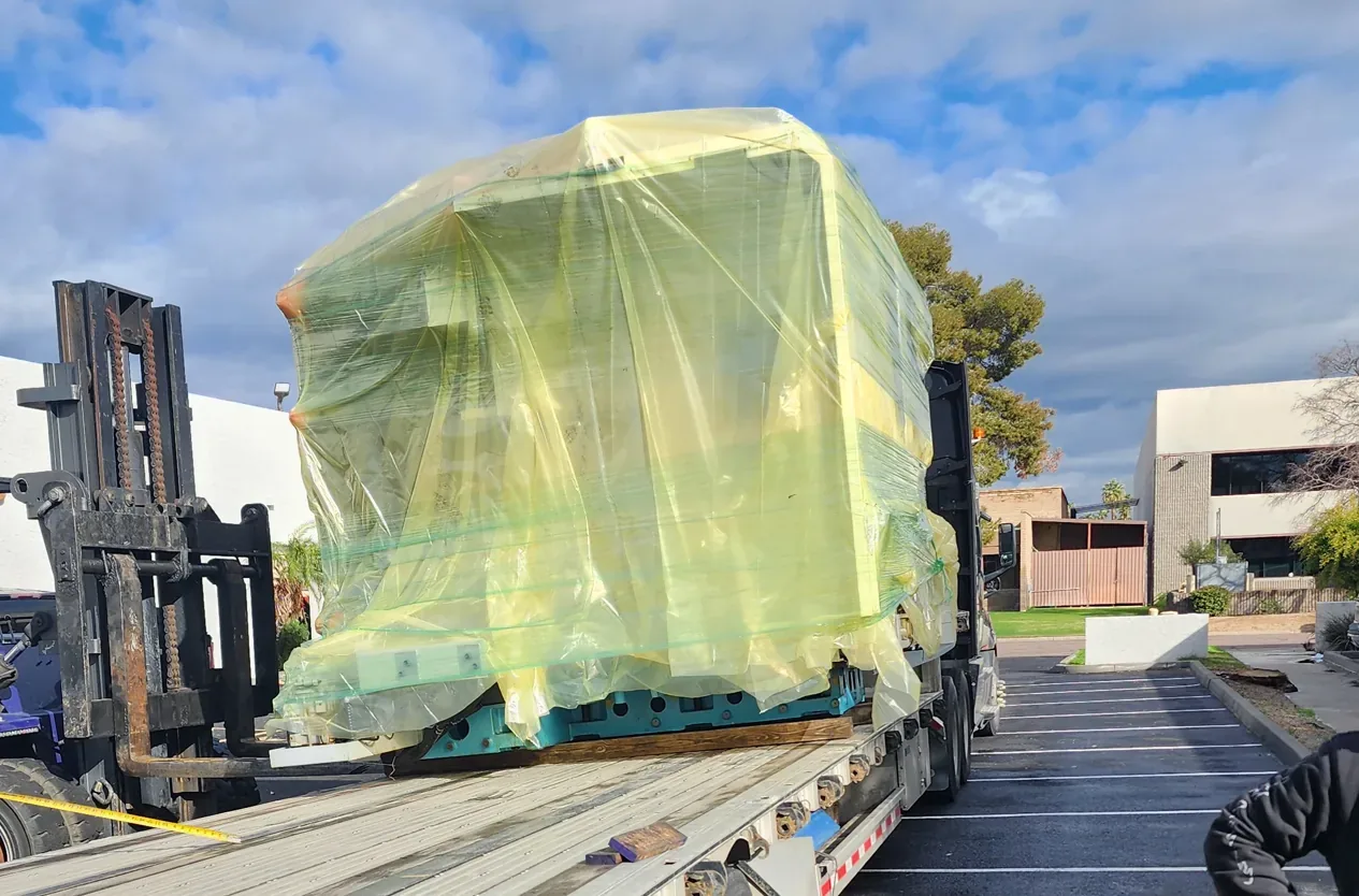 Forklift loading a wrapped machine onto a flatbed trailer