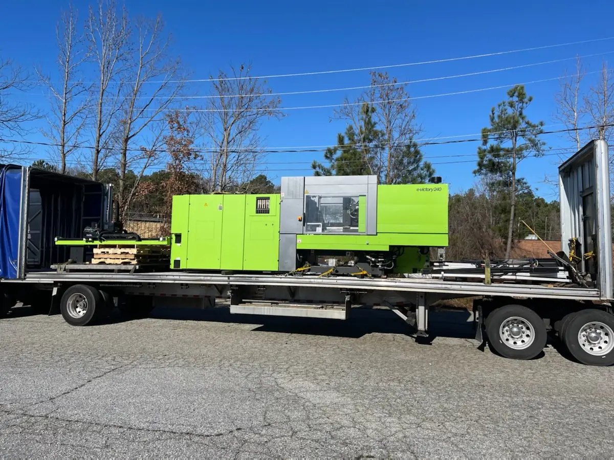 Green injection molding machine on a Conestoga flatbed trailer