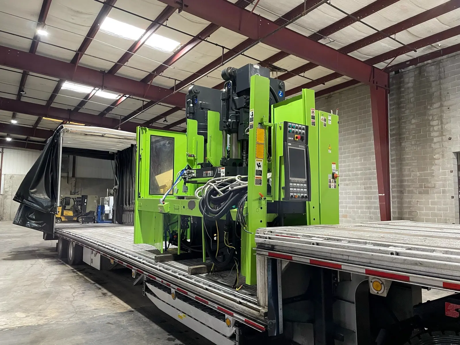 Green injection molding machine loaded on a Conestoga trailer in Los Angeles