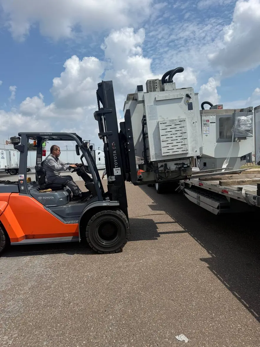 Forklift operator backing away from a step deck trailer with a Haas Mini Mill on the forks in Laredo, Texas