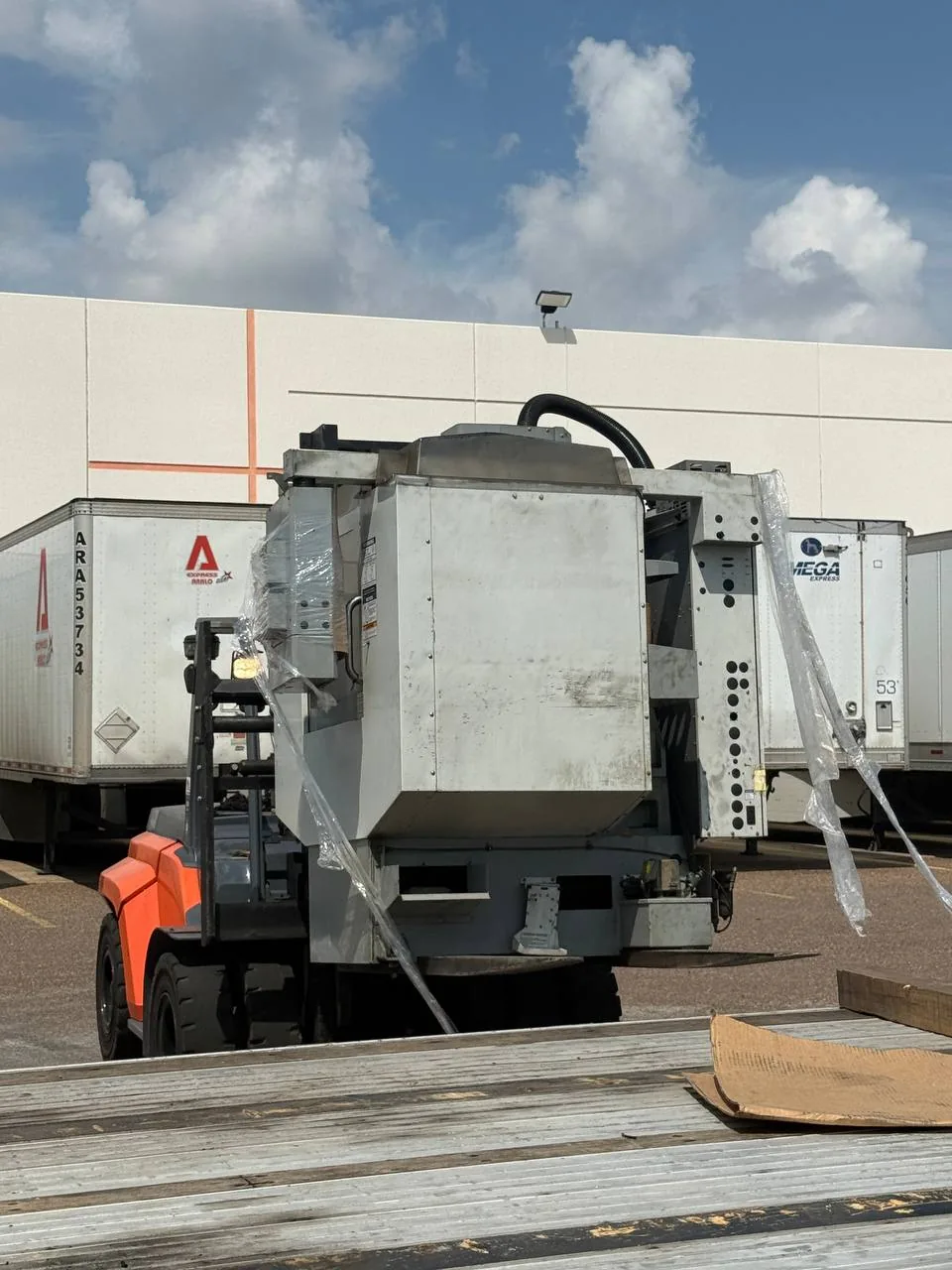 Forklift lifting the second Haas Mini Mill off the trailer with loose shrink wrap hanging from the machine