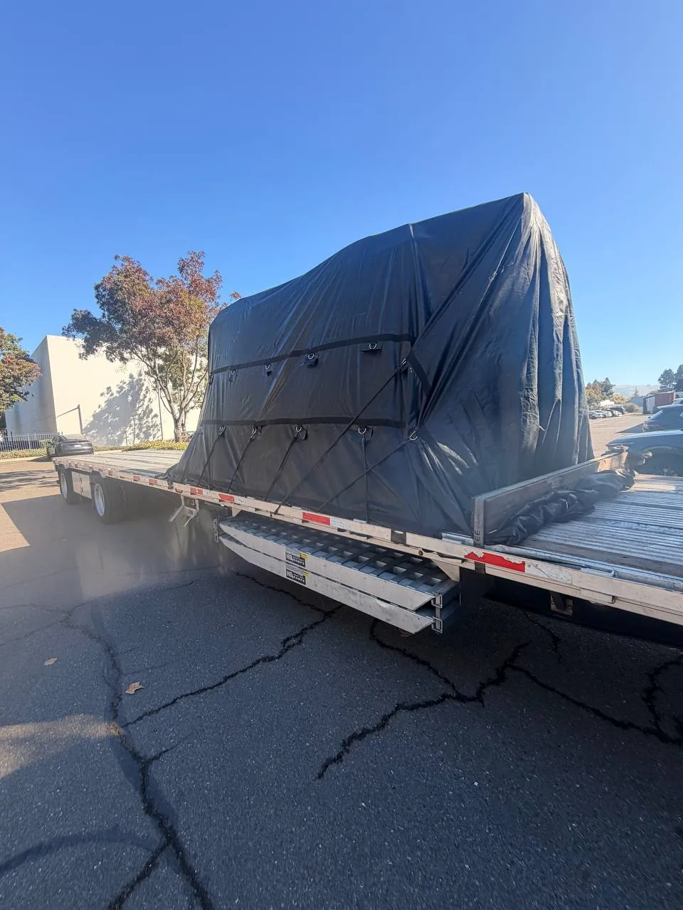 Two Haas Mini Mills fully covered with a black heavy-duty tarp on a step deck trailer at pickup