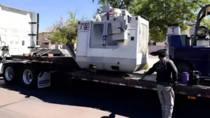 Haas VF-2 vertical mill on a rigger's flatbed parked on a neighborhood street as a crew member pulls a chain tight