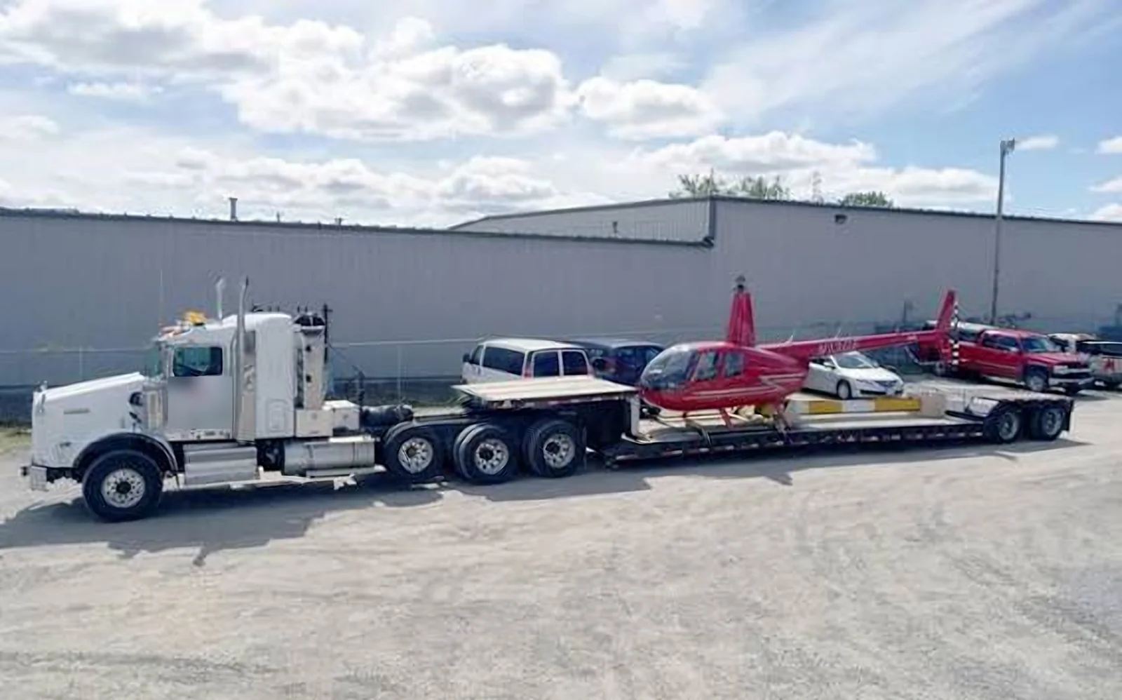 Helicopter Transport on a Lowboy Trailer Red helicopter secured on a lowboy trailer behind a white semi truck in a gravel lot