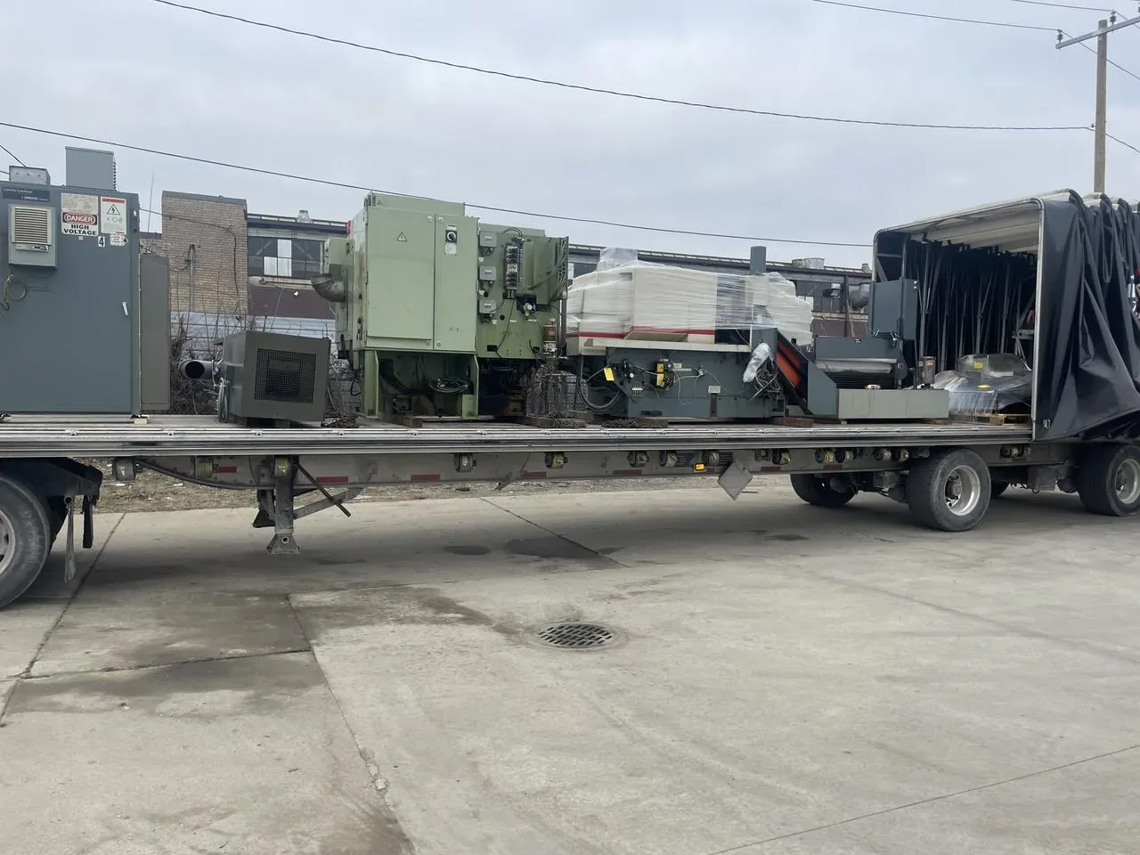 Several industrial machines on a Conestoga flatbed with the tarp kit rolled back