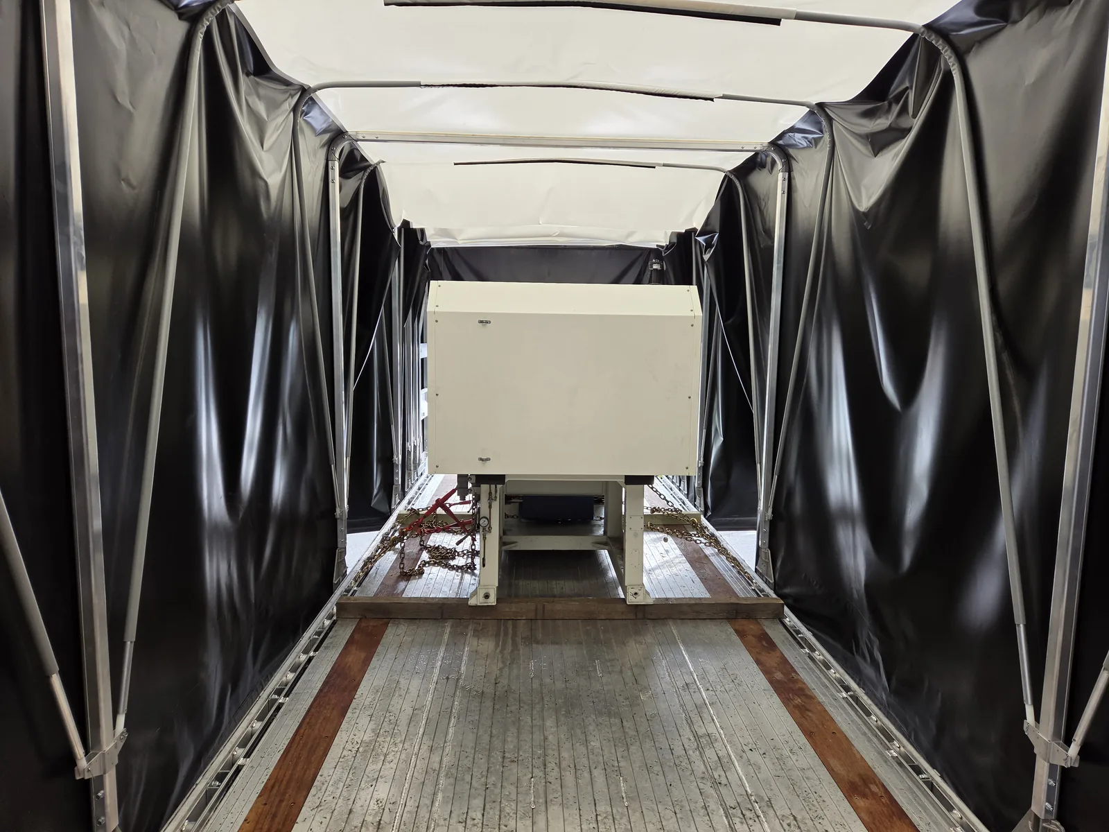 Injection molding machine chained on dunnage inside a Conestoga trailer