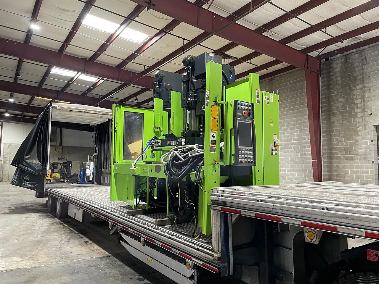 Injection Molder on a Flatbed Green injection molding machine on a flatbed in a warehouse
