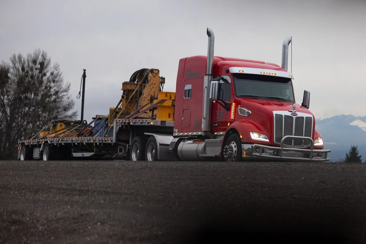 Red tractor pulling a step deck trailer loaded with yellow industrial machinery