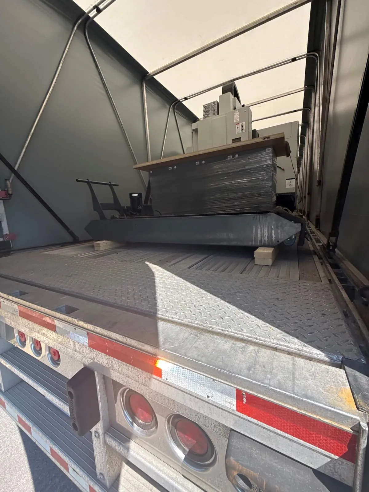 EDM machine on a steel skid inside a Conestoga trailer with the rolling tarp pulled back for EDM machine transport from Los Angeles