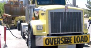 Yellow semi truck with an oversize load banner hauling a Caterpillar D9R crawler dozer on a lowboy trailer