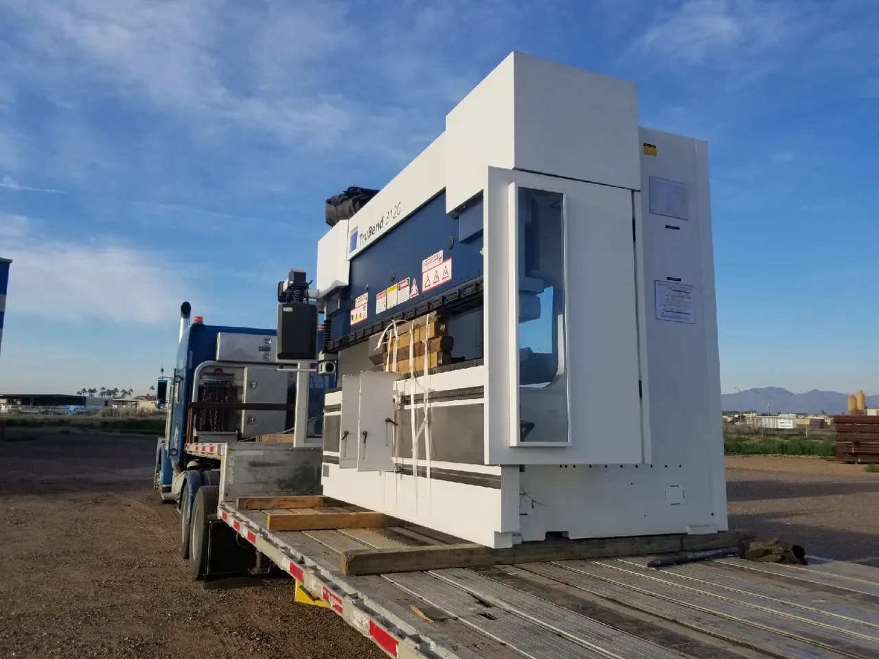 Press brake machine chained on a step deck trailer under a clear desert sky