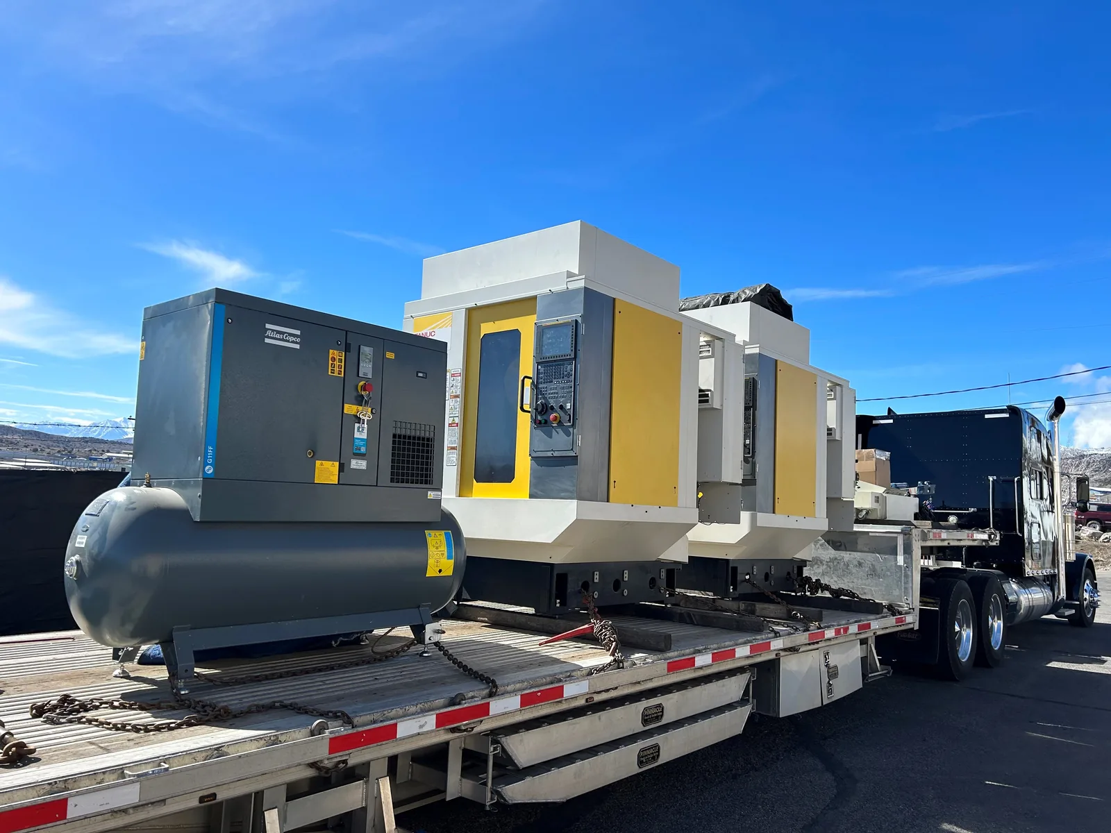 Fanuc machining centers and an Atlas Copco air compressor chained on a flatbed for a machinery dealer move from Los Angeles