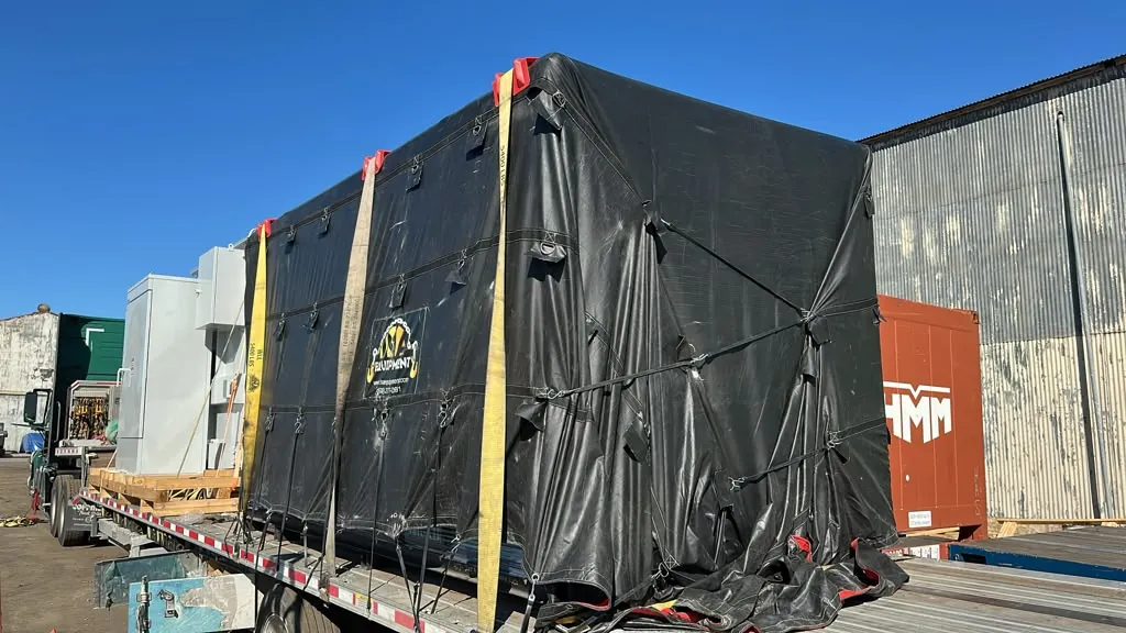 Machine crate covered with a black tarp and yellow straps on a step deck trailer bound for Texas