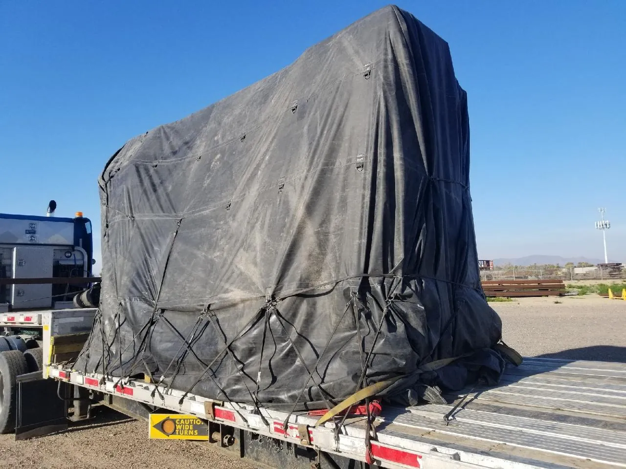 Tarped Machinery on a Flatbed Trailer Tall machine covered with a black tarp and strapped on a flatbed trailer