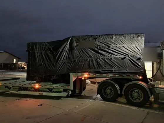 Tarped load on a step deck trailer parked at night under a dark sky