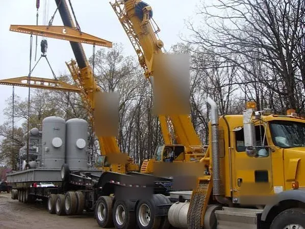 Two mobile cranes with spreader bars lifting pressure vessels onto a multi axle trailer