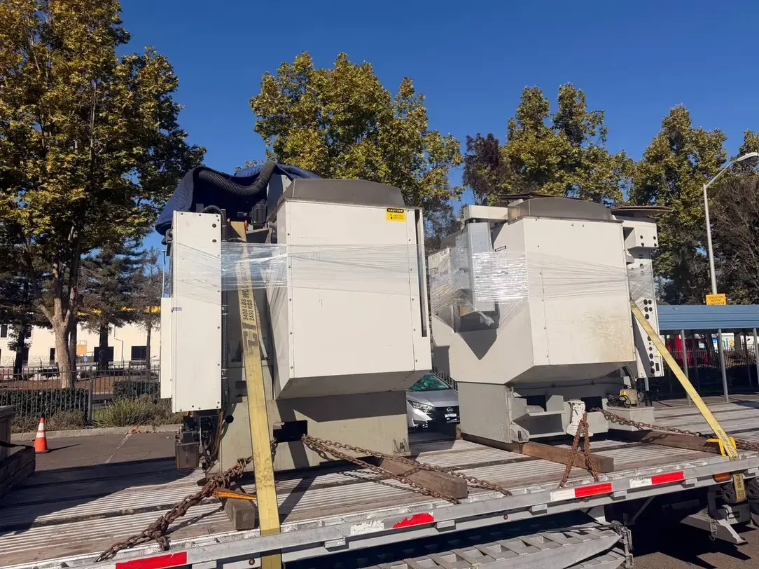 Two shrink wrapped vertical machining centers chained on wood dunnage on a step deck